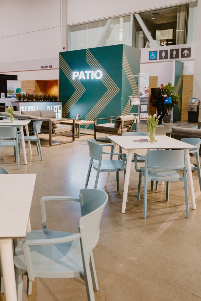 A seating area with white tables, each have a small vase of white flowers and light blue armchairs surrounding it