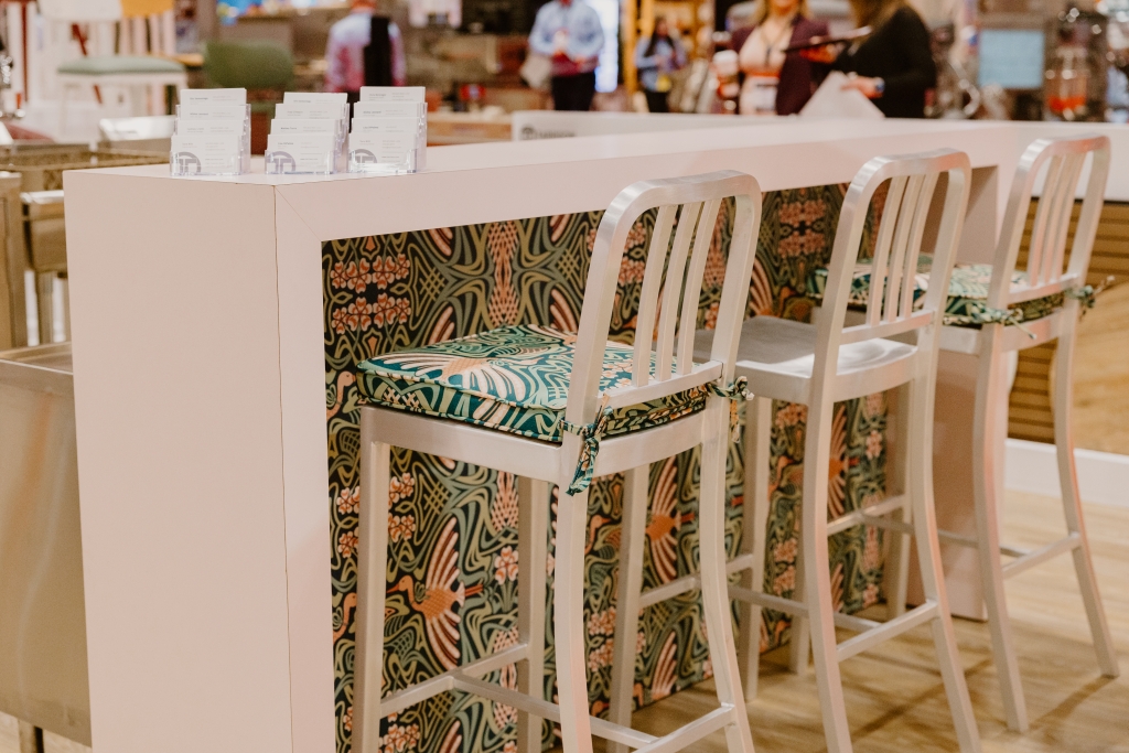 Aluminum barstools against a light pink bar with a brightly coloured floral pattern featuring pink birds. Two of the barstools have cushions with the same pattern