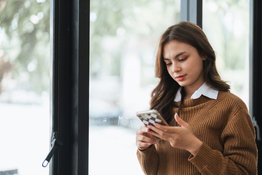 A woman in a brown sweater holding and using a mobile phone