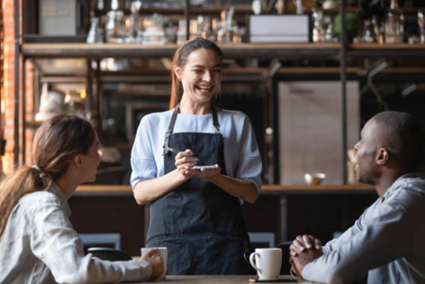 Smiling server takes the orders of two customers at a cafe